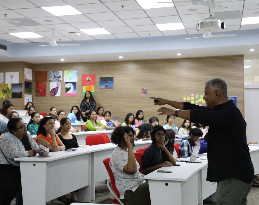 This is a carousel image which shows a blurred image of an orientation session which shows the speaker addressing a large audience.